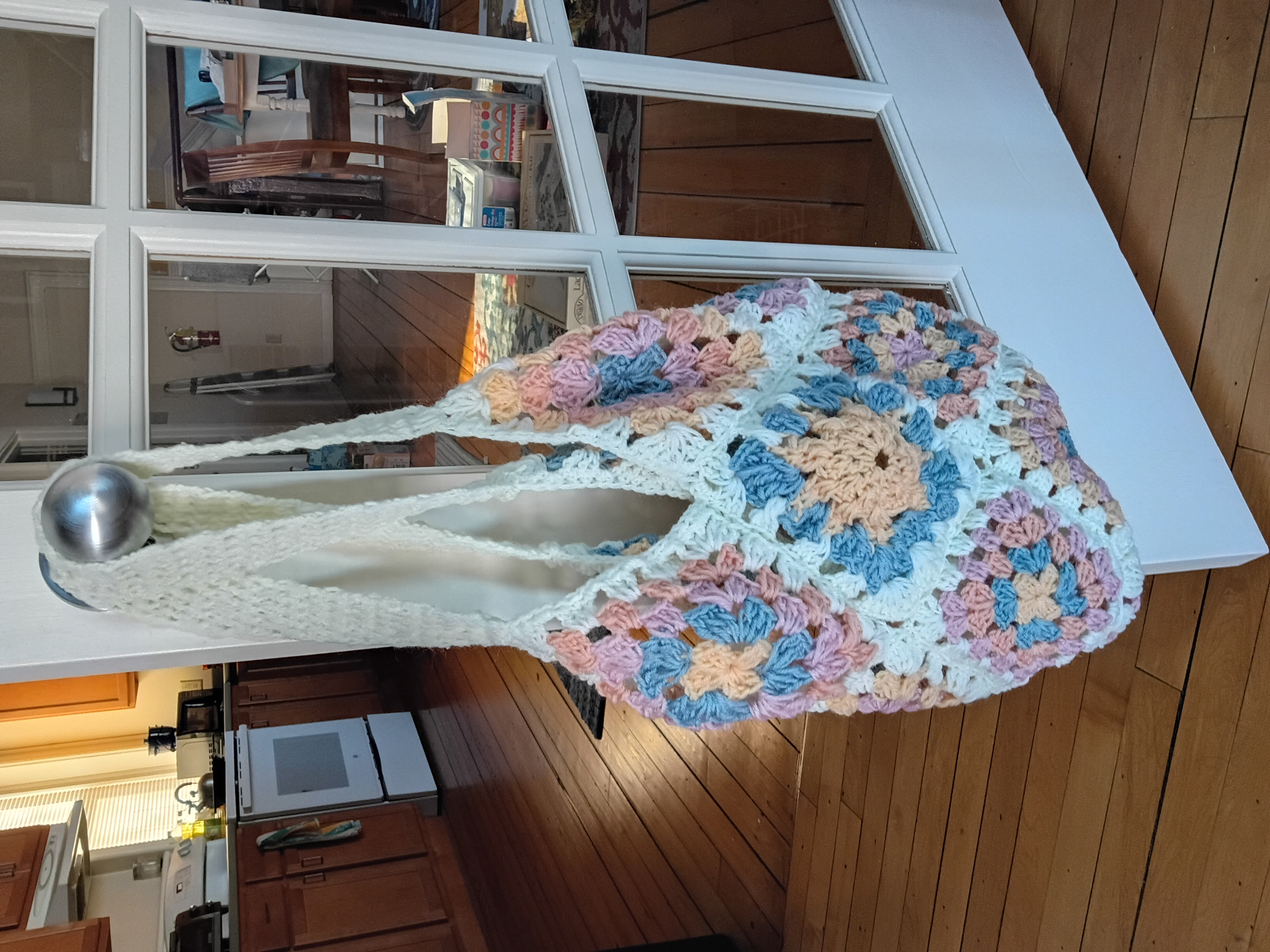 a colorful crochet bag hanging from the handle of a glass door